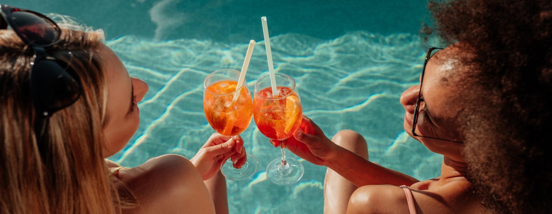 a couple people holding drinks sitting by the pool